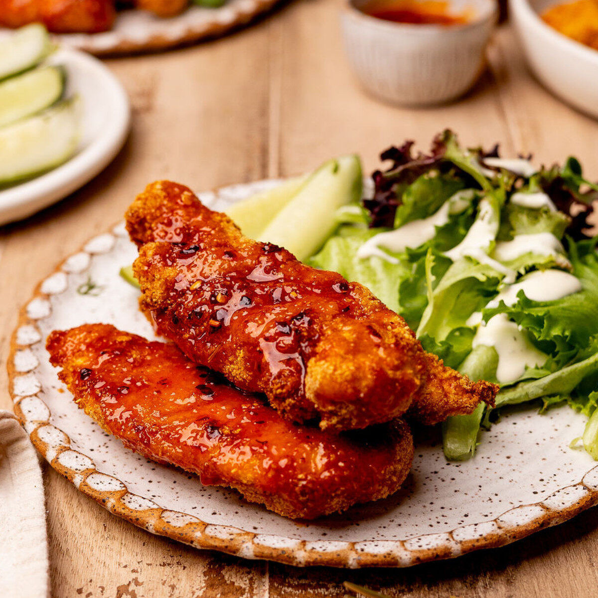 Air fryer hot honey chicken tenders on a plate with a side salad and pickles.
