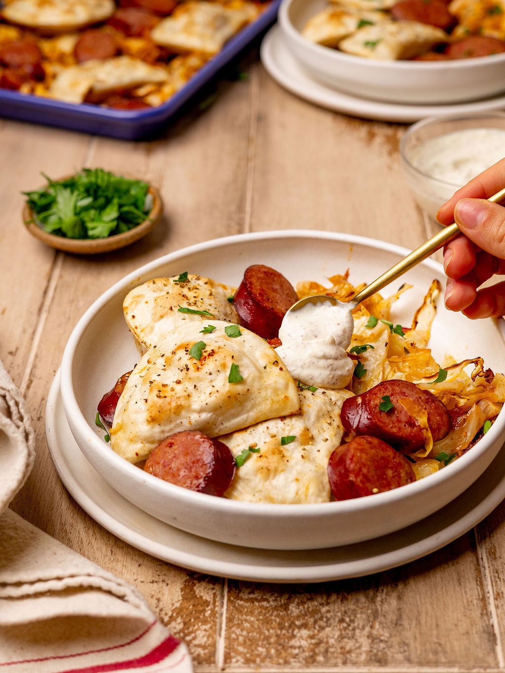 Adding a dollop of sour cream to a plate of pierogi and kielbasa.