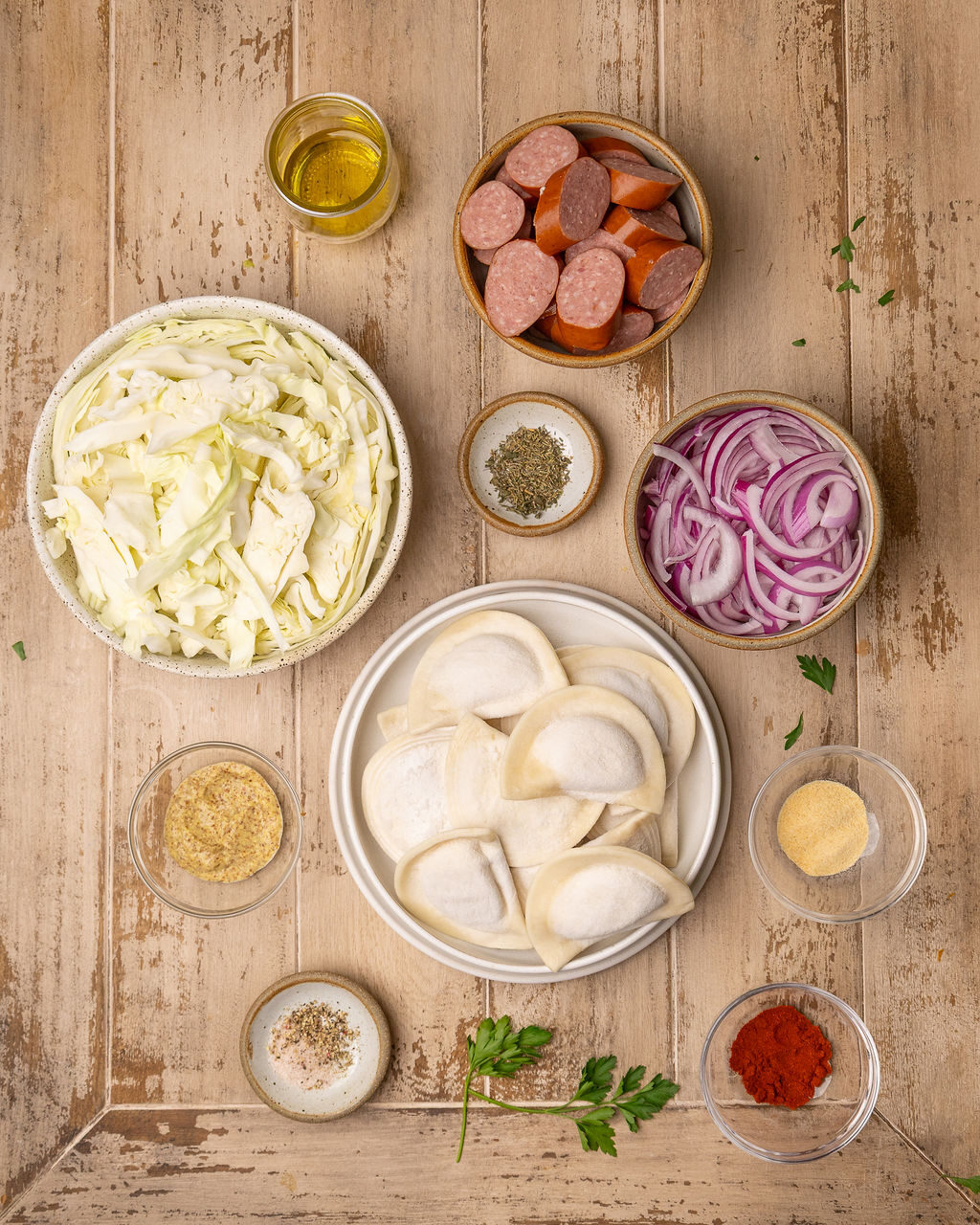 Ingredients for pierogi and kielbasa sheet pan dinner on a light wooden surface.
