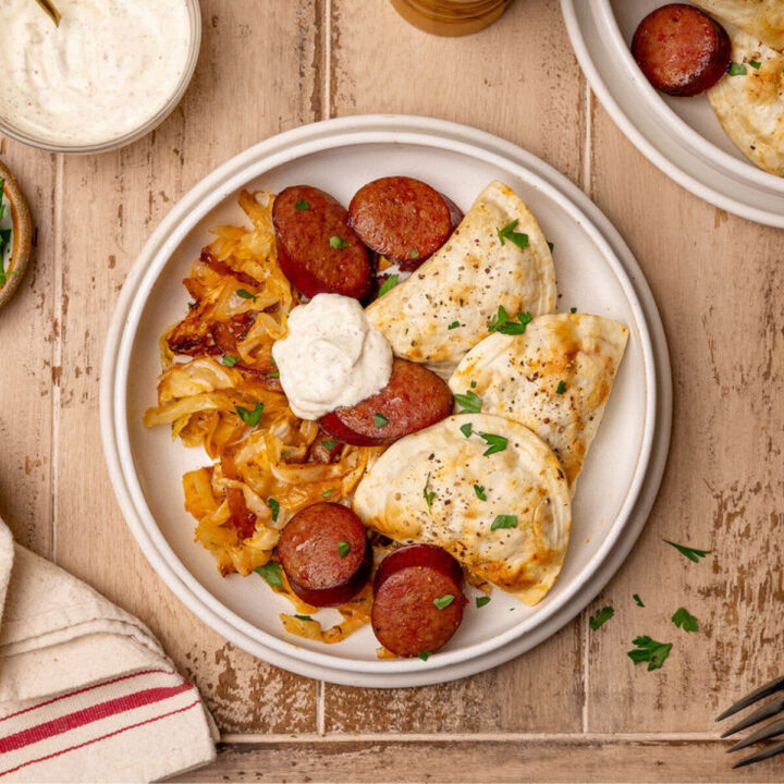 Pierogi and kielbasa sheet pan dinner on a white plate with a dollop of sour cream.