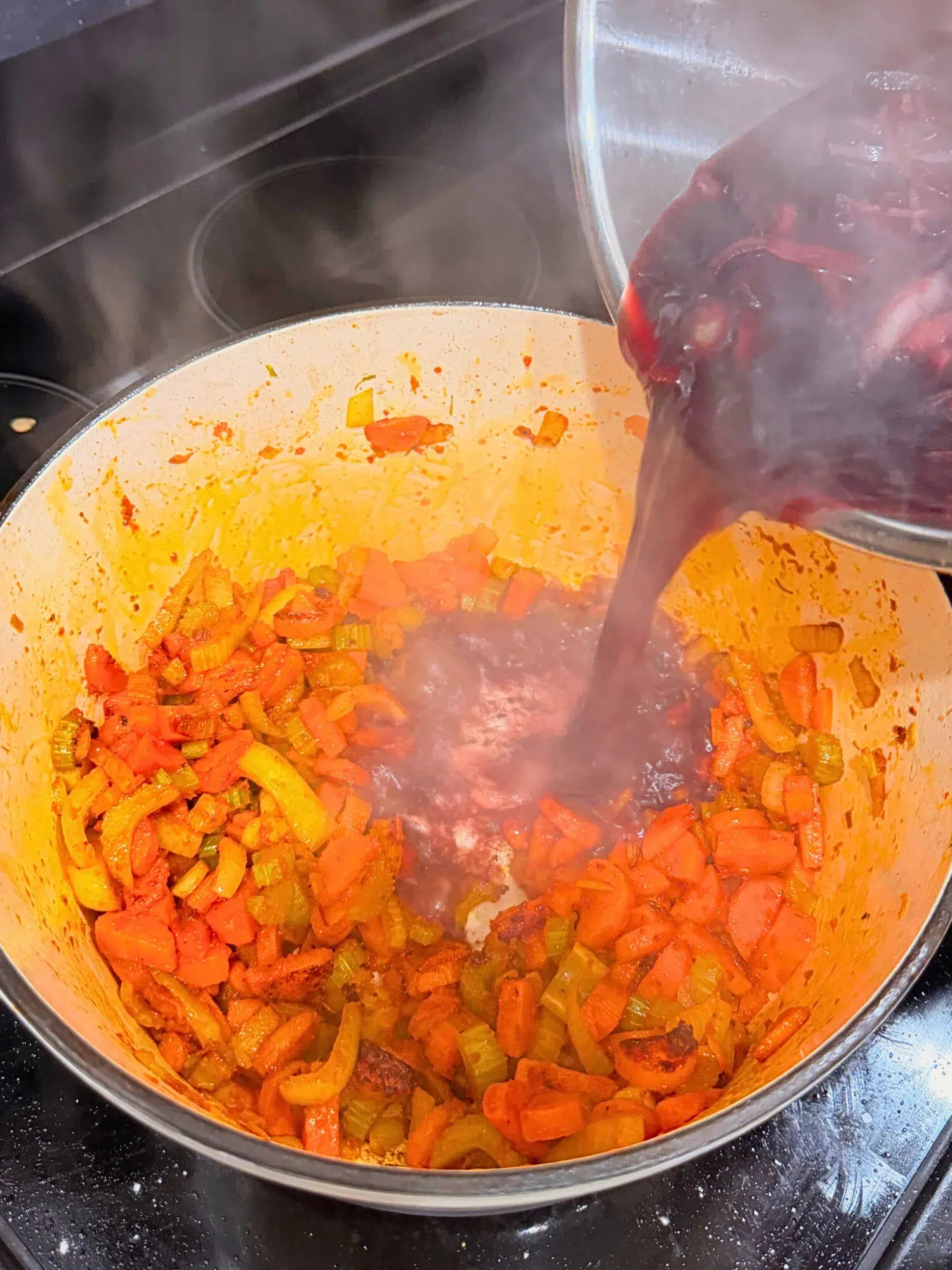 Adding wine to a Dutch oven filled with sauteed veggies.