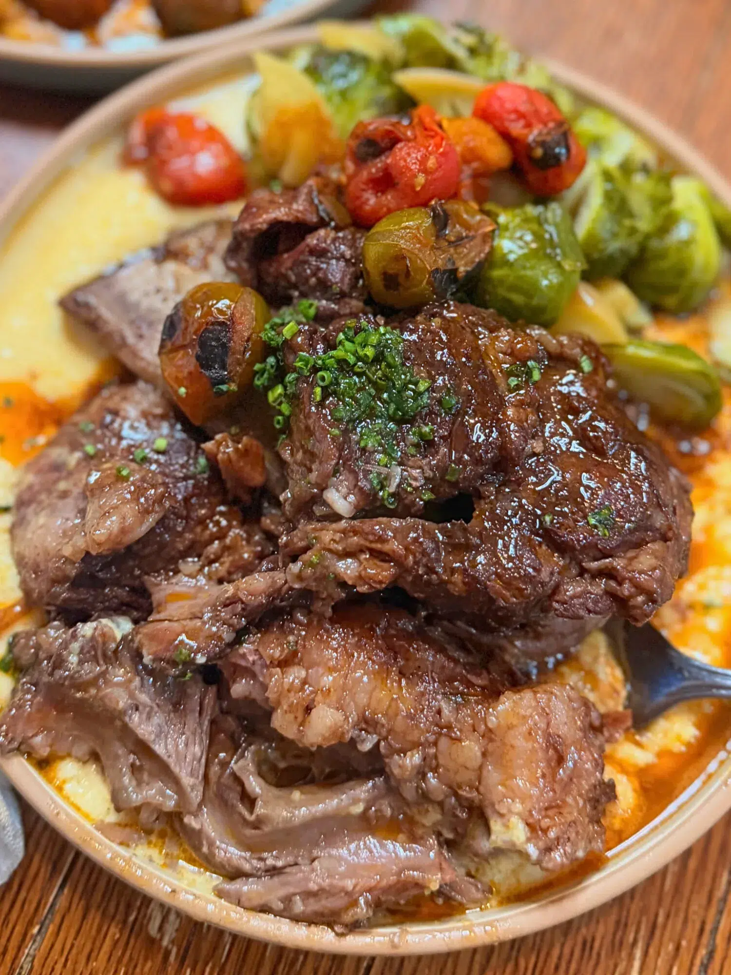 Close-up of short ribs over polenta with a side of roasted veggies.