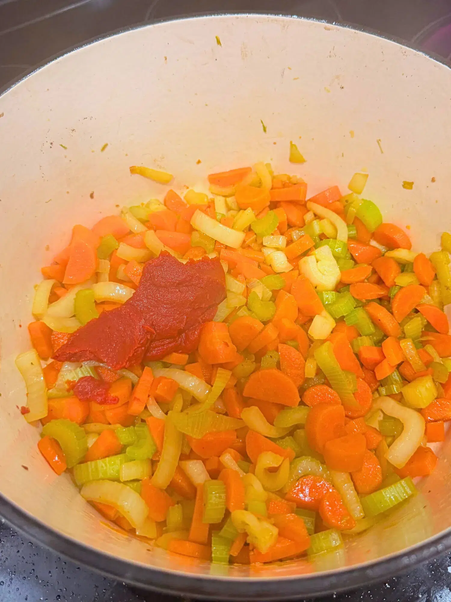 Adding tomato paste to a Dutch oven of sauteed veggies.