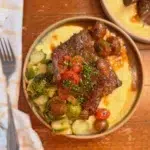 Short ribs in a bowl with polenta, cherry tomatoes, and brussels sprouts.
