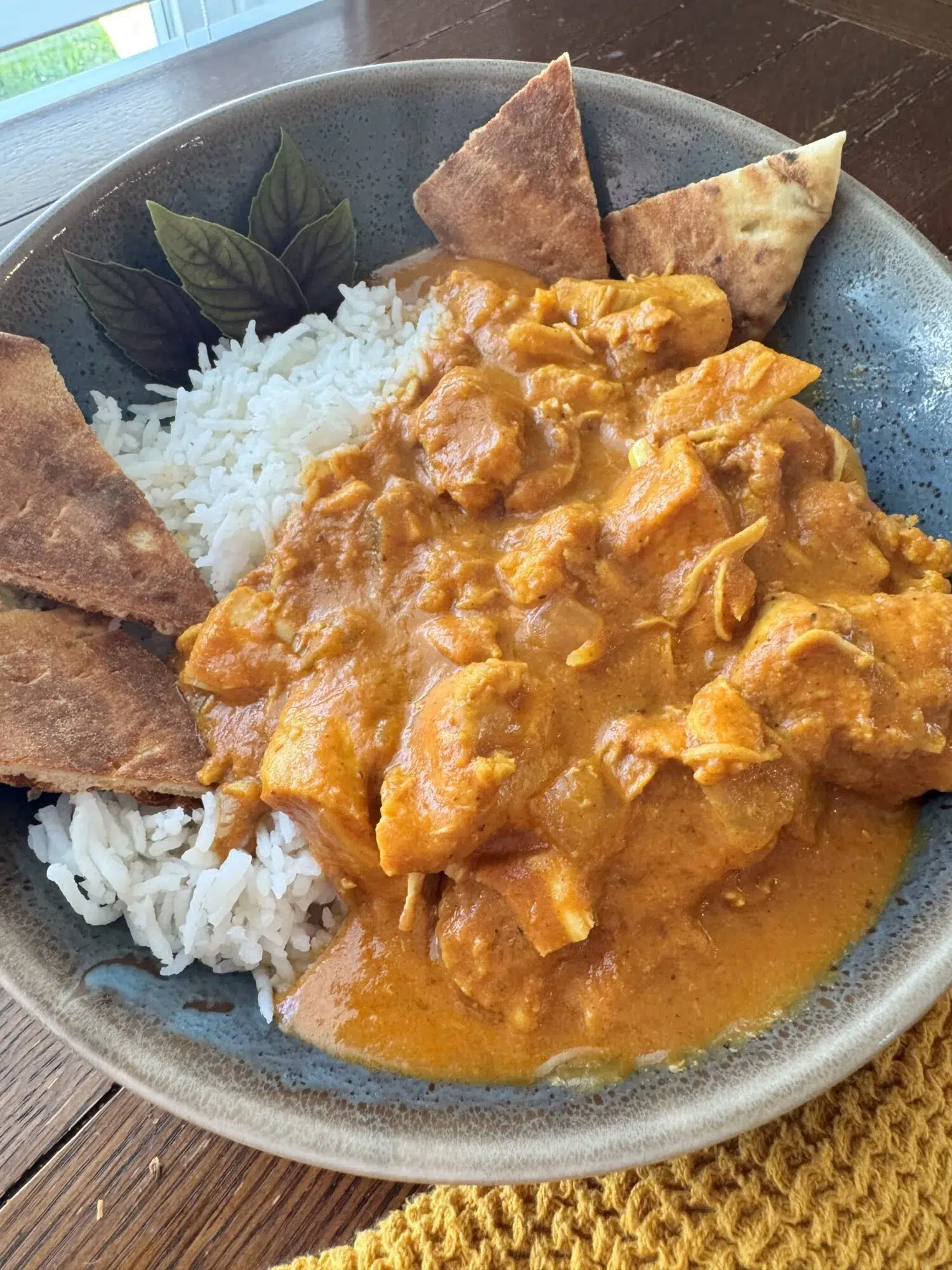Close-up of a bowl of butter chicken over rice with naan.