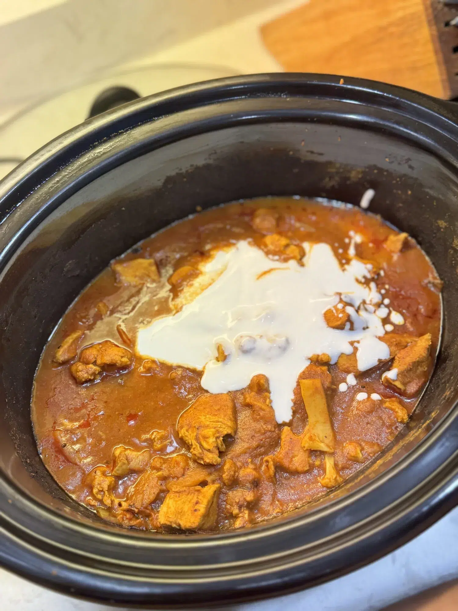 Adding coconut milk to a crock pot of butter chicken.