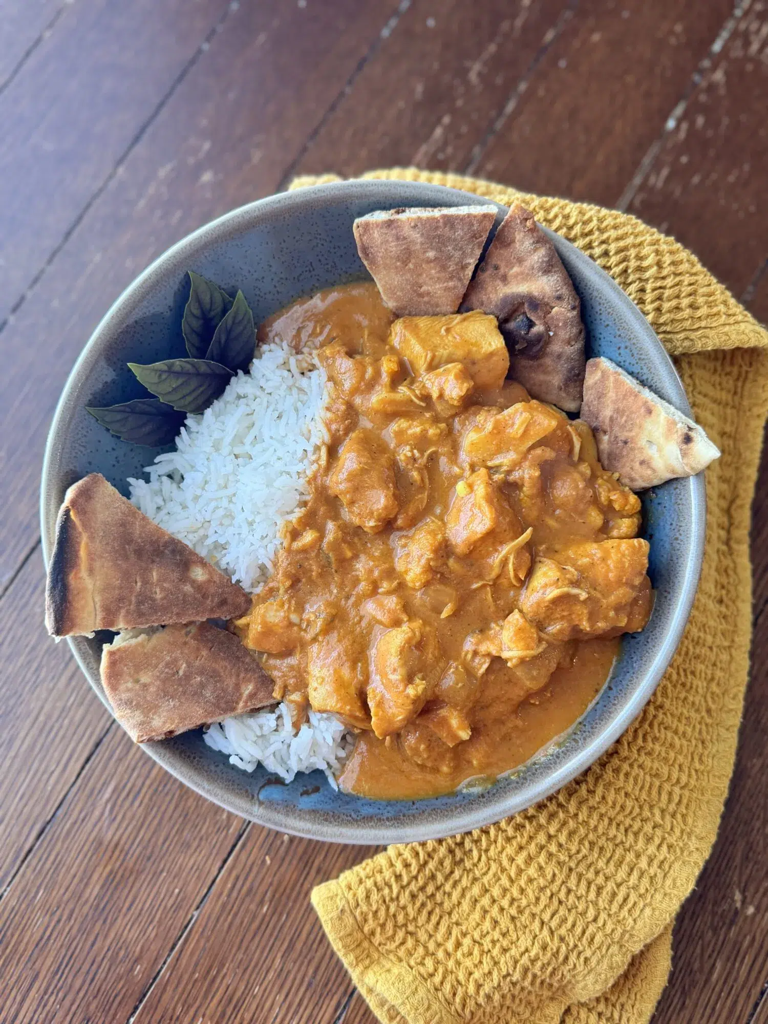 A serving of slow cooker butter chicken over rice with naan.