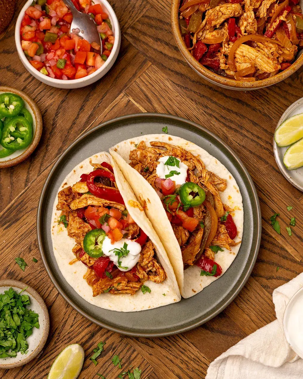 Slow cooker fajitas on a black plate surrounded by ingredients.