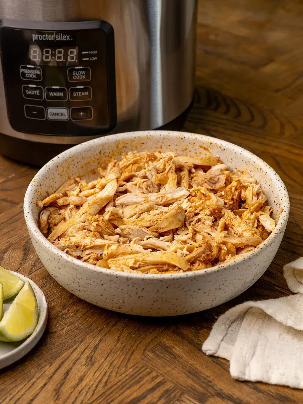 Shredded chicken in a white bowl in front of a slow cooker.