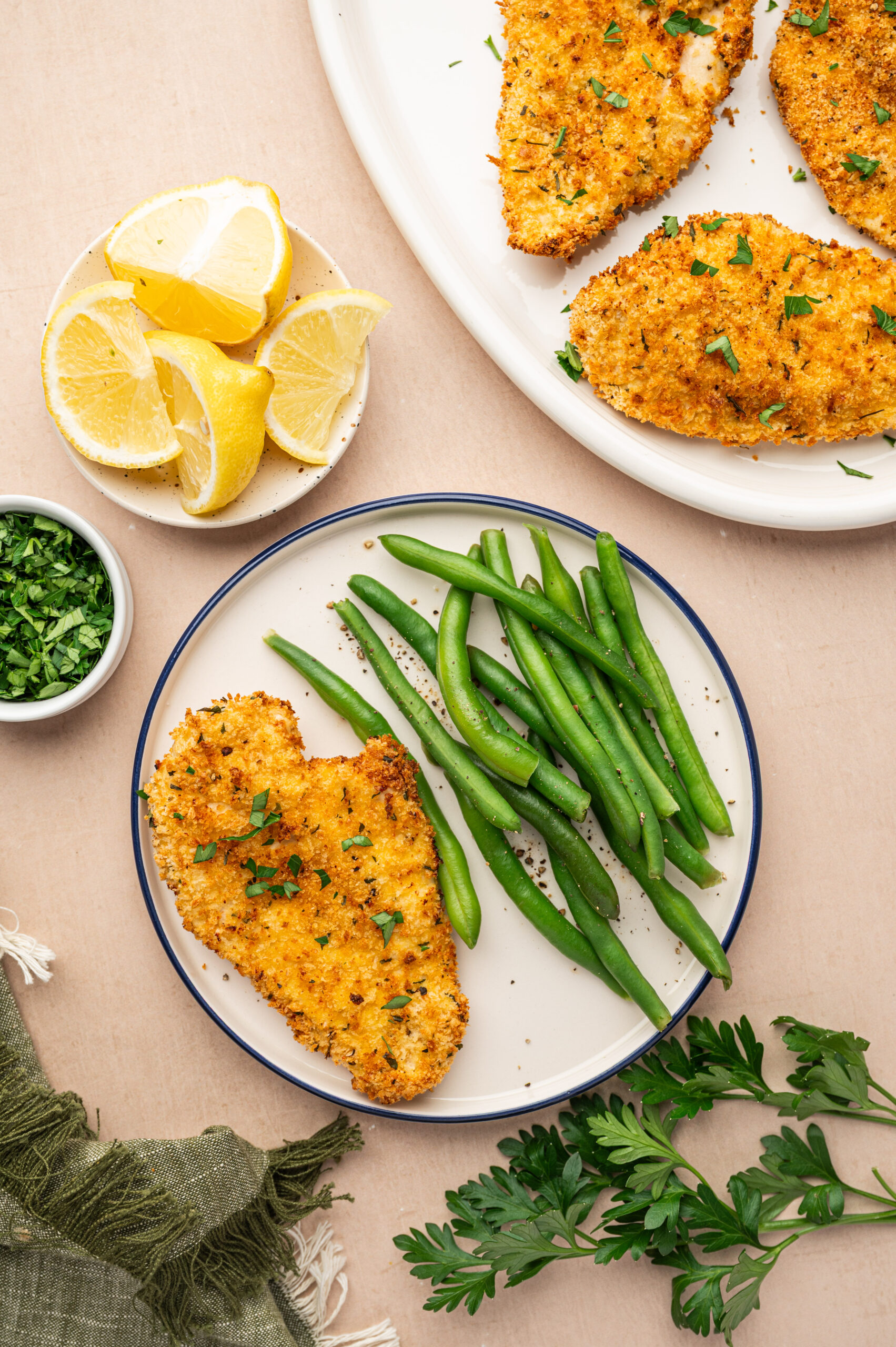 A breaded chicken cutlet on a white plate with a side of green beans surrounded by ingredients.
