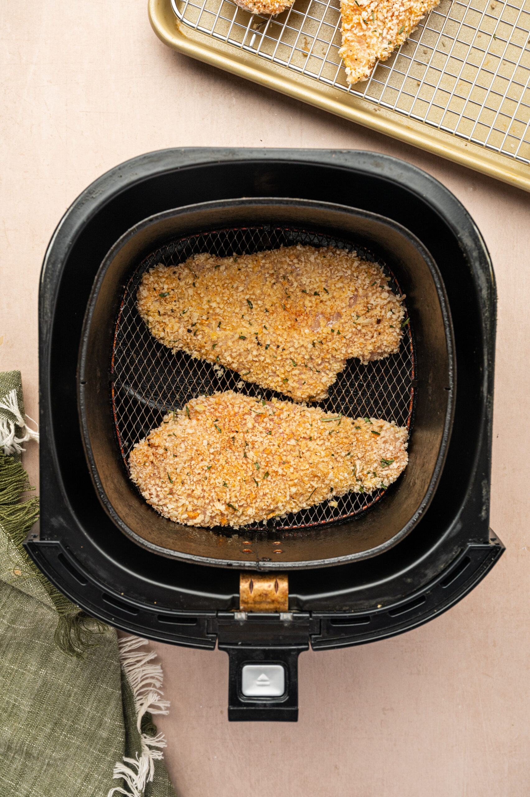 Breaded, uncooked chicken cutlets in an air fryer basket ready to cook.