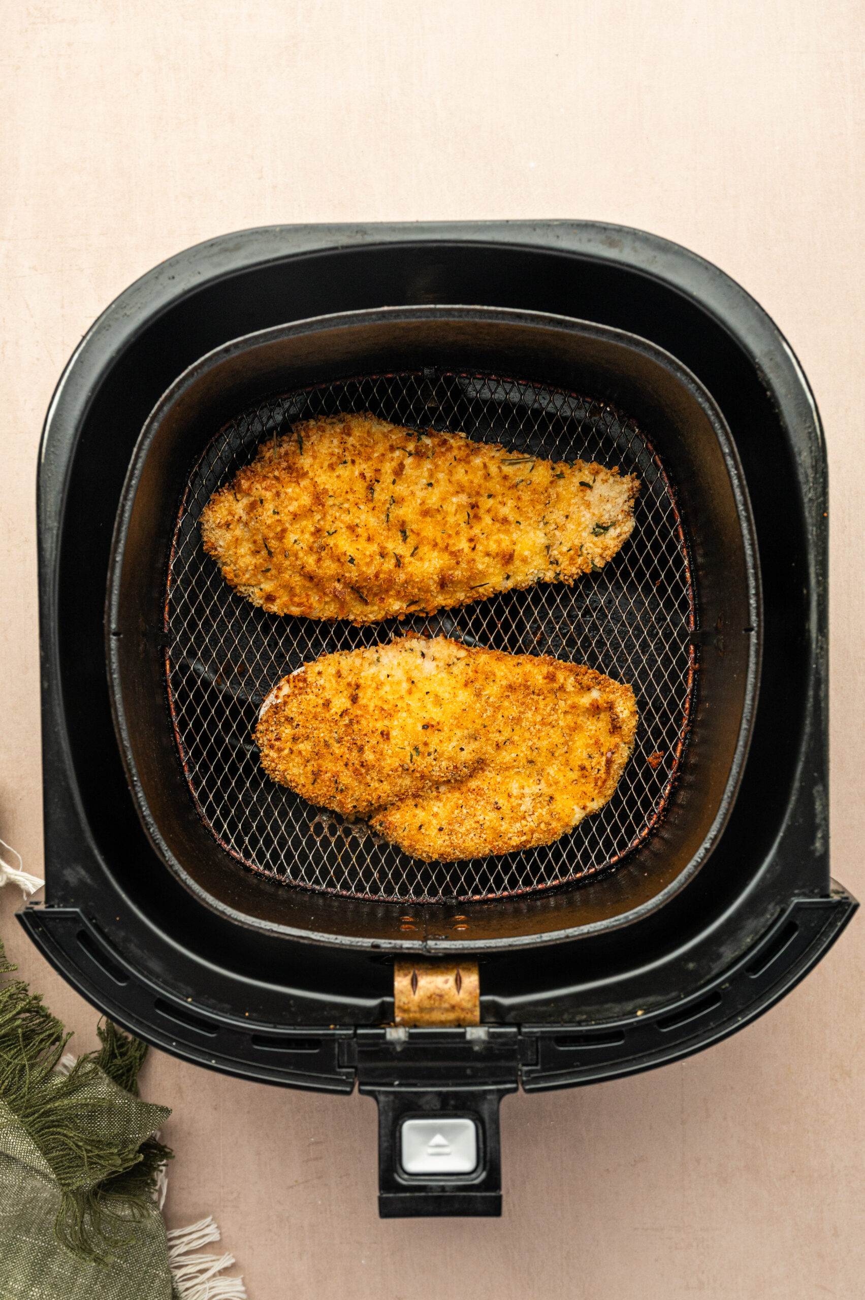 Cooked chicken cutlets in an air fryer basket.