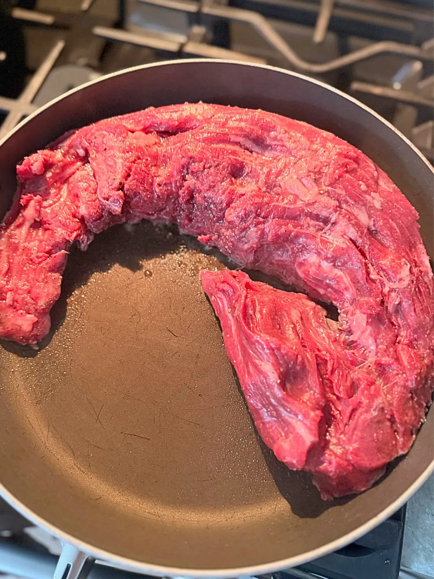 Raw beef tenderloin searing in a skillet.