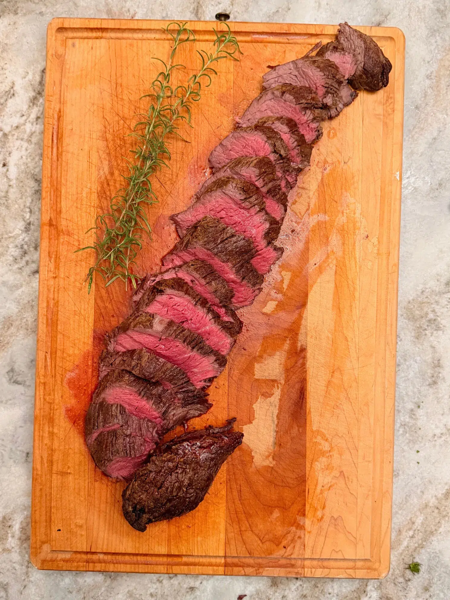 Sliced beef tenderloin on a cutting board with fresh thyme sprigs.