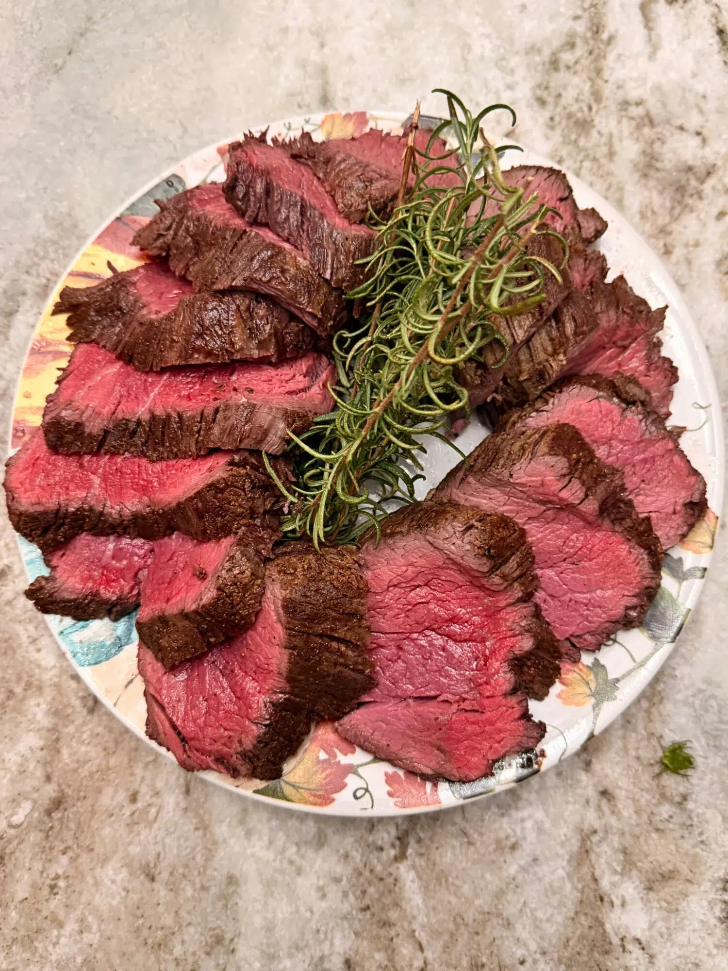 Sliced beef tenderloin presented on a plate with fresh thyme sprigs.