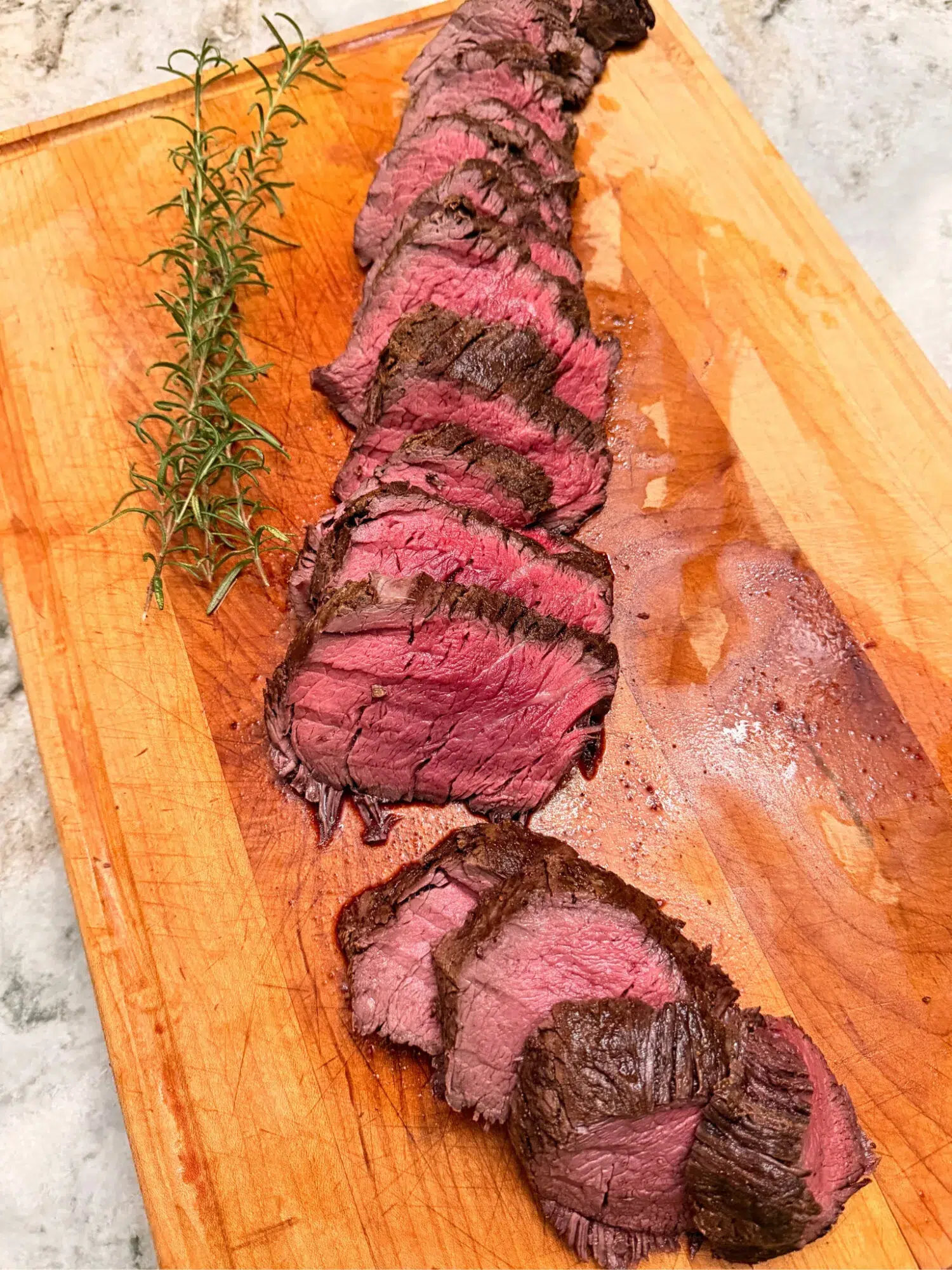 Sliced beef tenderloin on a cutting board with fresh thyme sprigs.