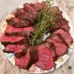Sliced beef tenderloin presented on a plate with fresh thyme sprigs.