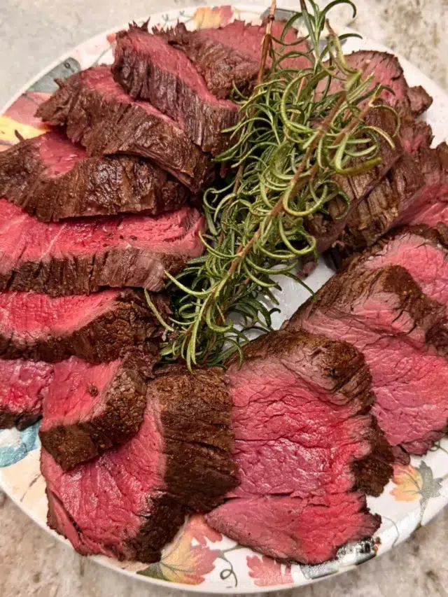 Sliced beef tenderloin presented on a plate with fresh thyme sprigs.