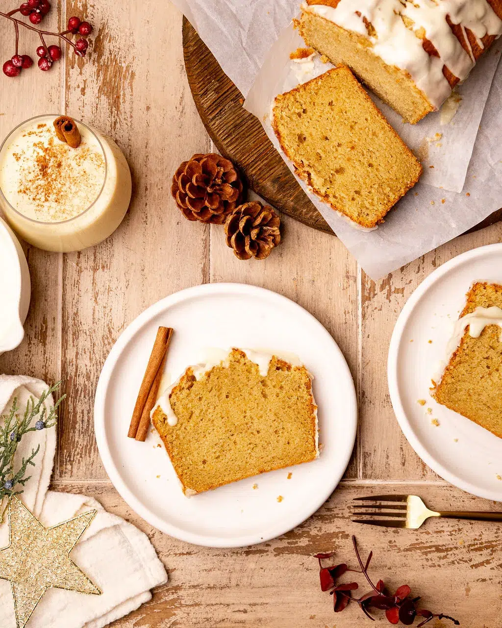 Plates of eggnog bread on a light wooden surface surrounded by ingredients.