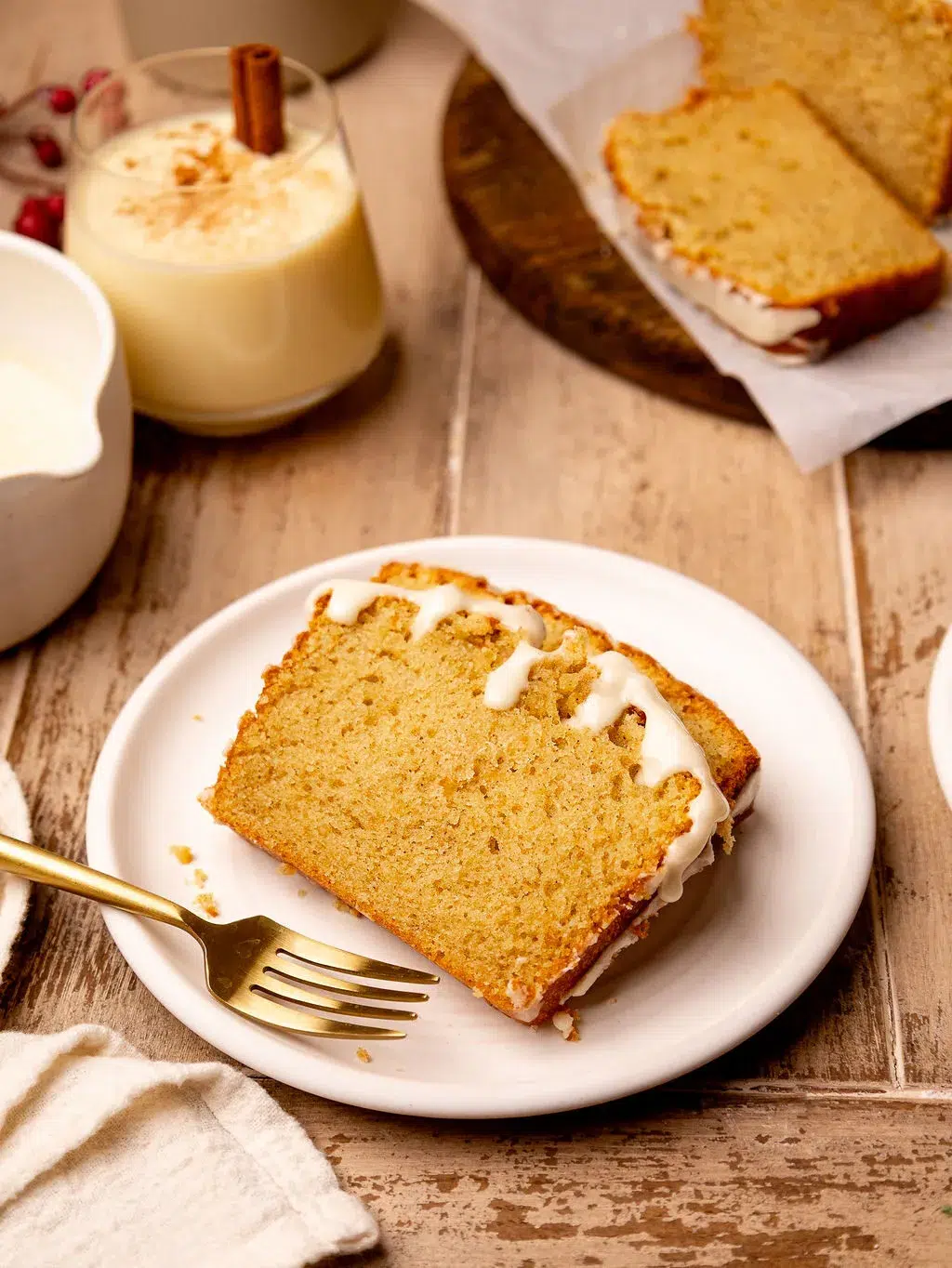 Two slices of eggnog bread on a white plate surrounded by ingredients.