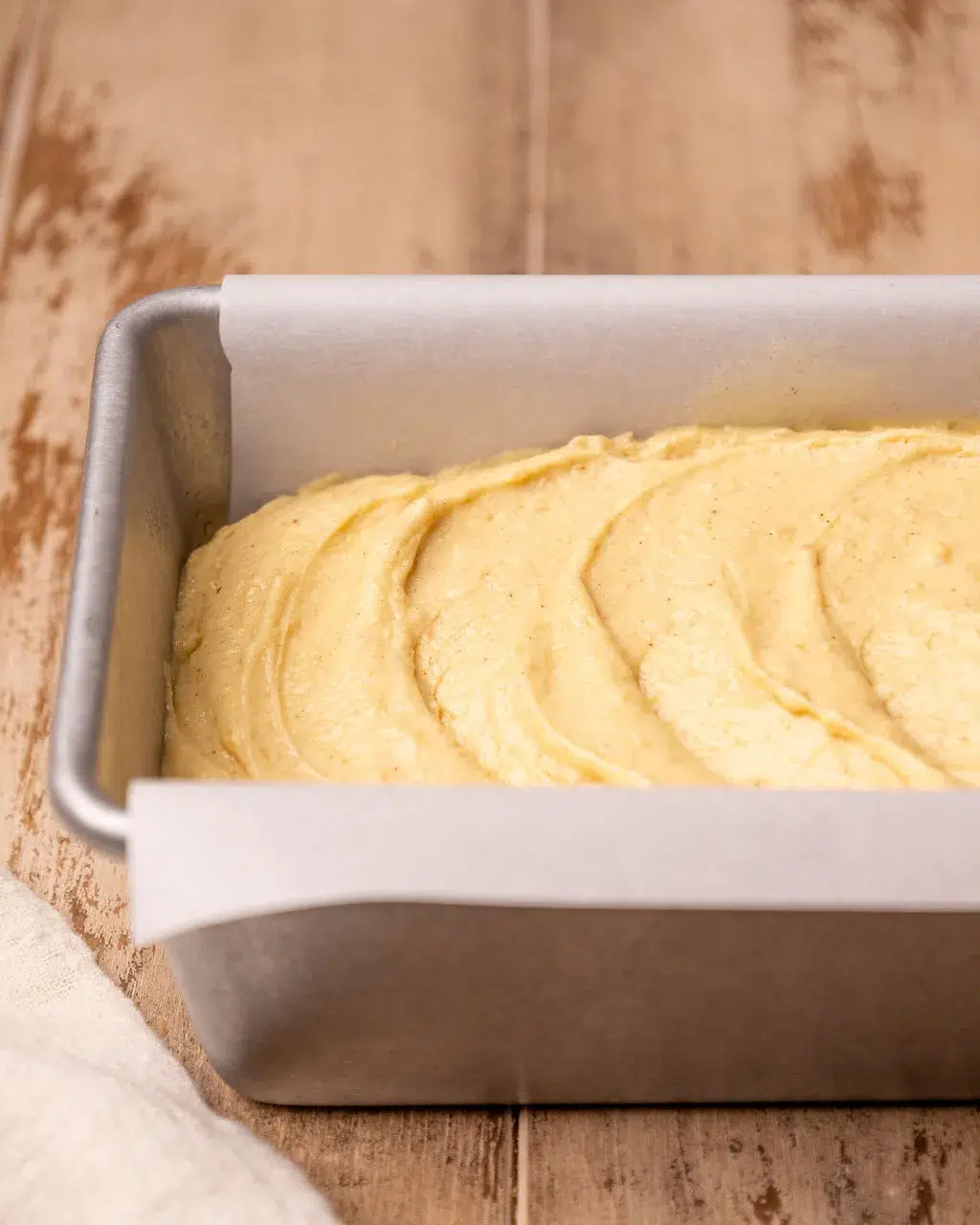 Batter for eggnog bread in a loaf pan lined with parchment paper.