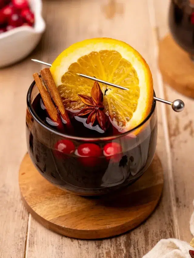 Slow cooker mulled wine garnished with star anise, a cinnamon stick, orange slice, and cranberries.
