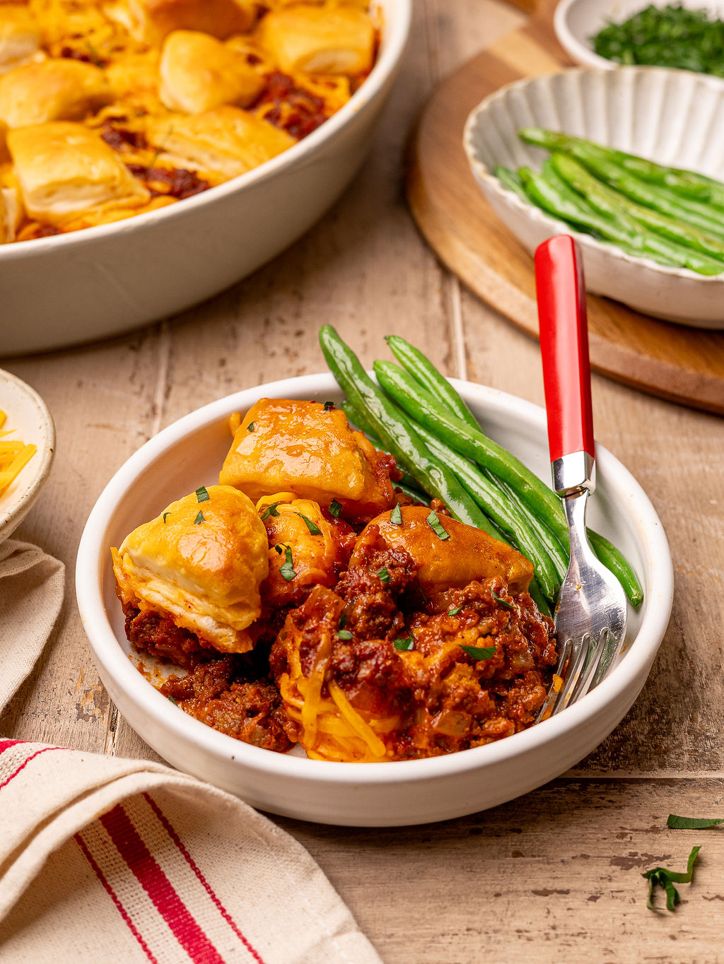 A white bowl of sloppy joe biscuit bake with a side of green beans.