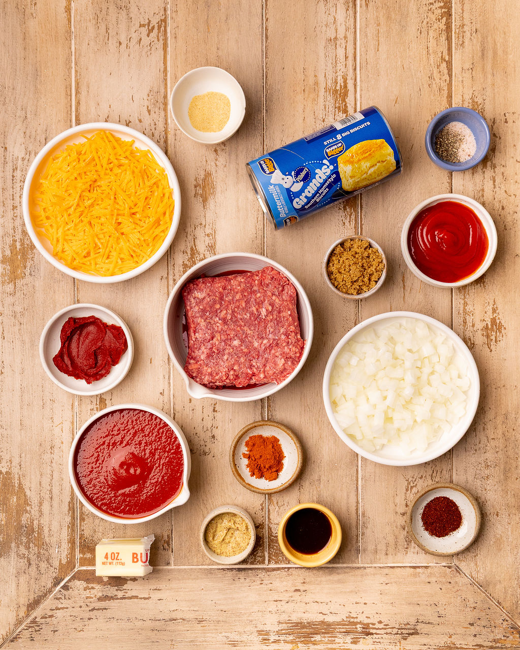 Ingredients for sloppy joe biscuit bake over a light wooden surface.