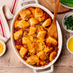 Sloppy joe biscuit bake in a baking dish over a rustic wooden surface.