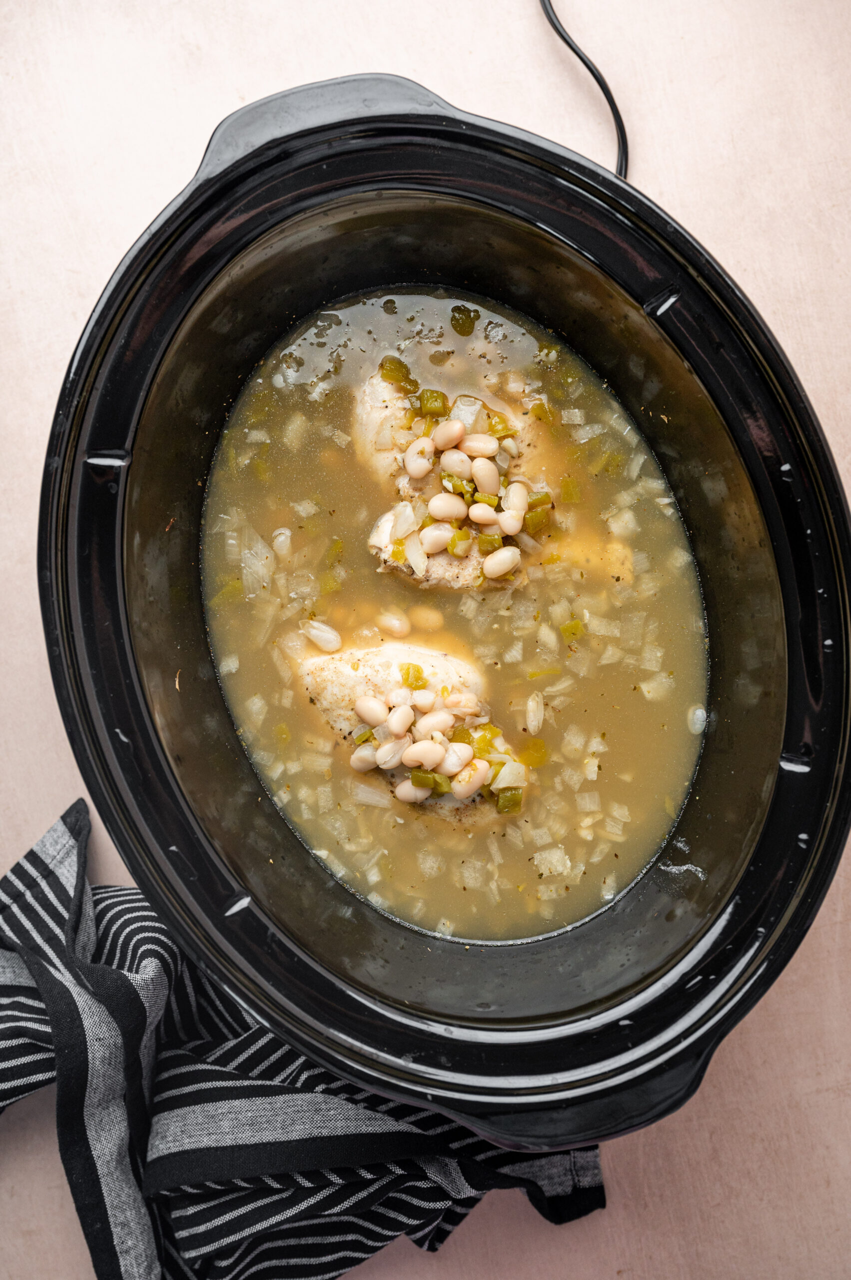Cooked chicken, onions, and broth inside a slow cooker.