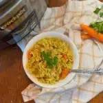 A bowl of chicken noodle soup next to a slow cooker.