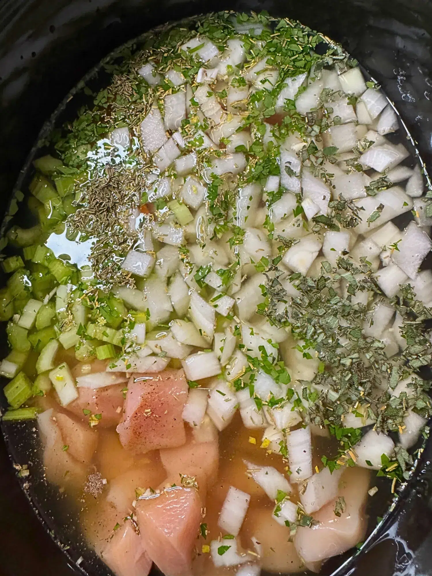 Chicken, onion, and herbs in a slow cooker.