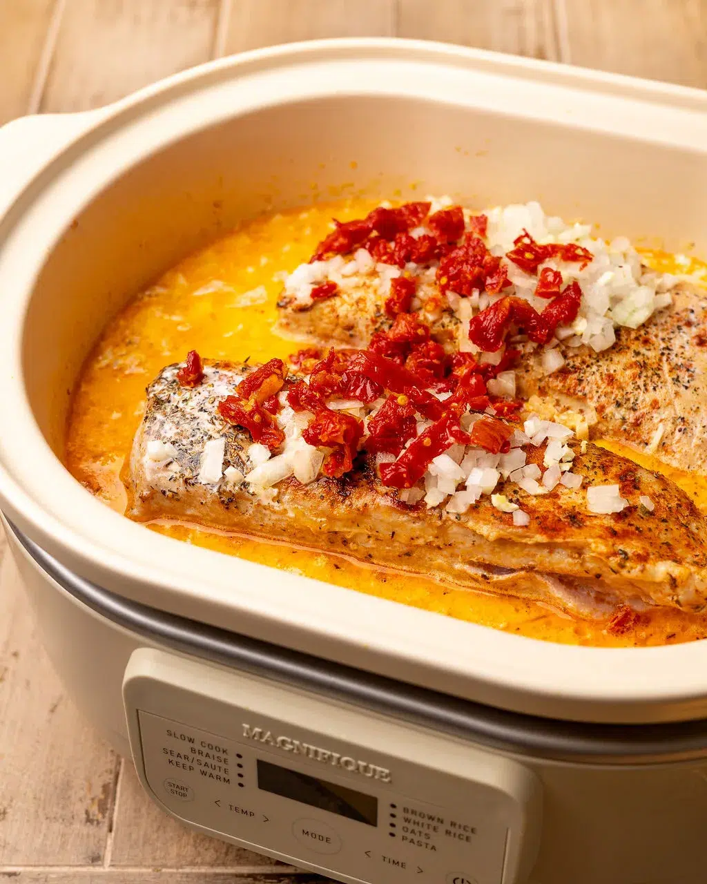Adding sun-dried tomatoes and parmesan to a slow cooker of Tuscan sauce.