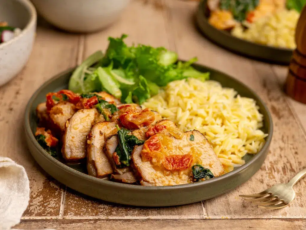 A serving of slow cooker Tuscan pork tenderloin topped with sauce with a side of rice and greens.