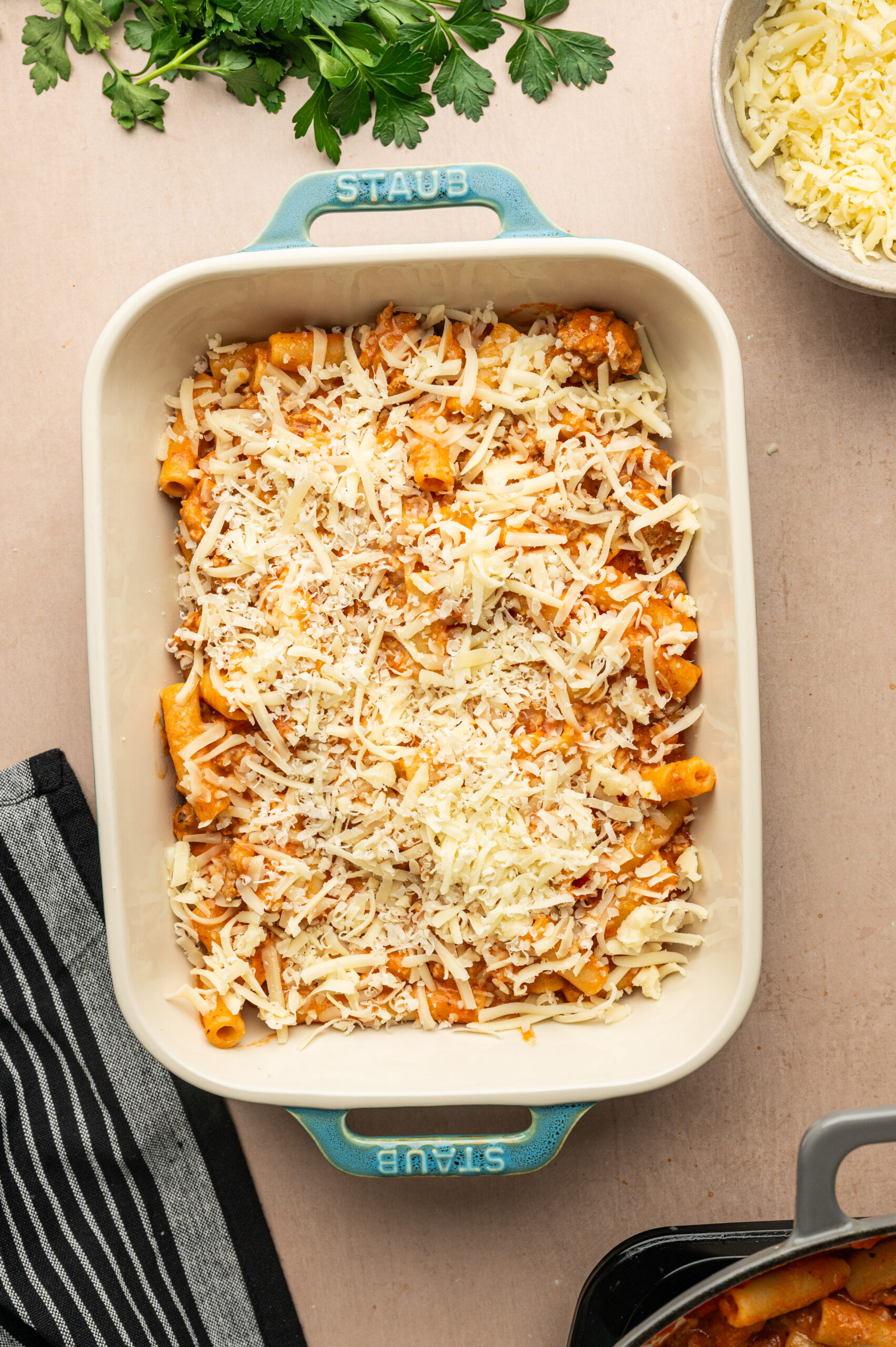 Layering cheese over cooked ziti in a casserole dish.