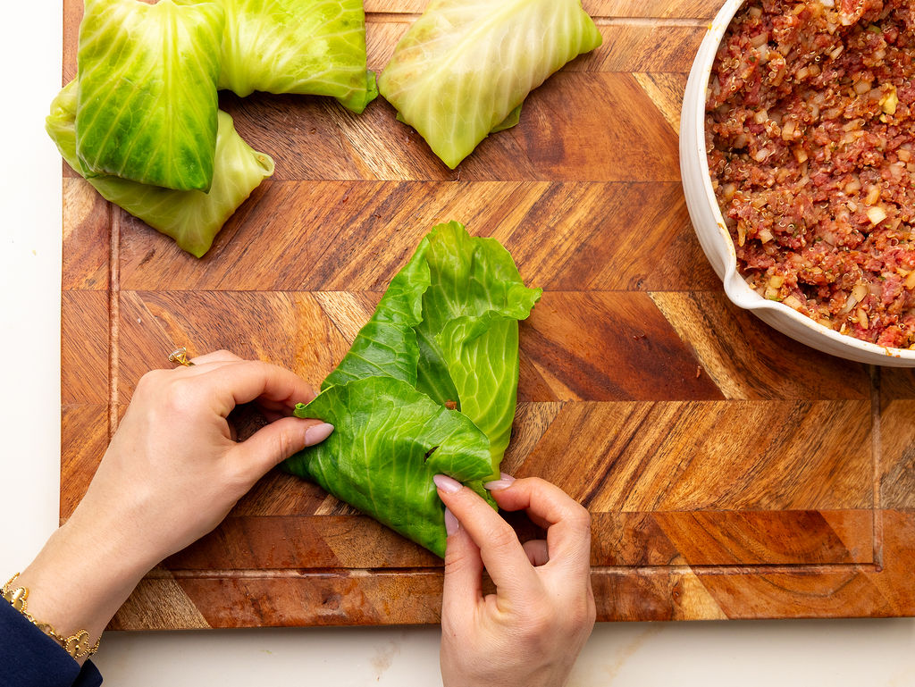 Rolling a lean beef stuffed cabbage roll on a cutting board.