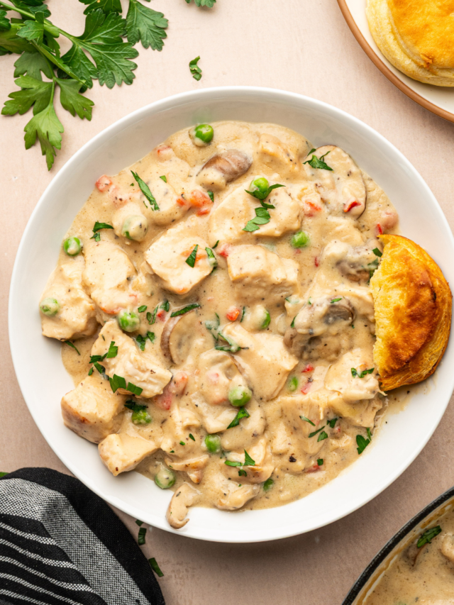 A bowl of chicken a la king in a white bowl garnished with fresh parsley and served with biscuits.