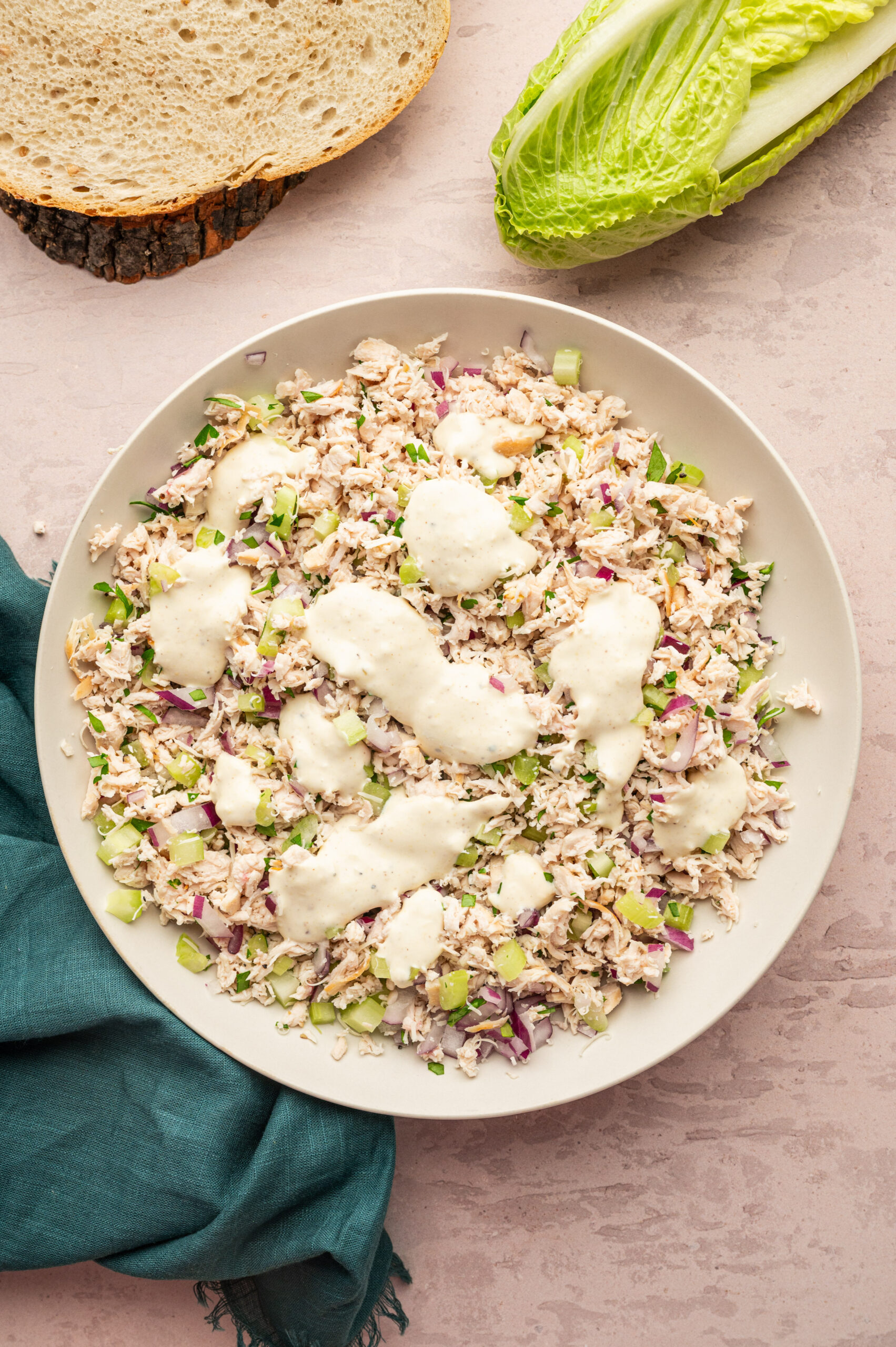 Adding dressing to a bowl of shredded chicken and chopped veggies.