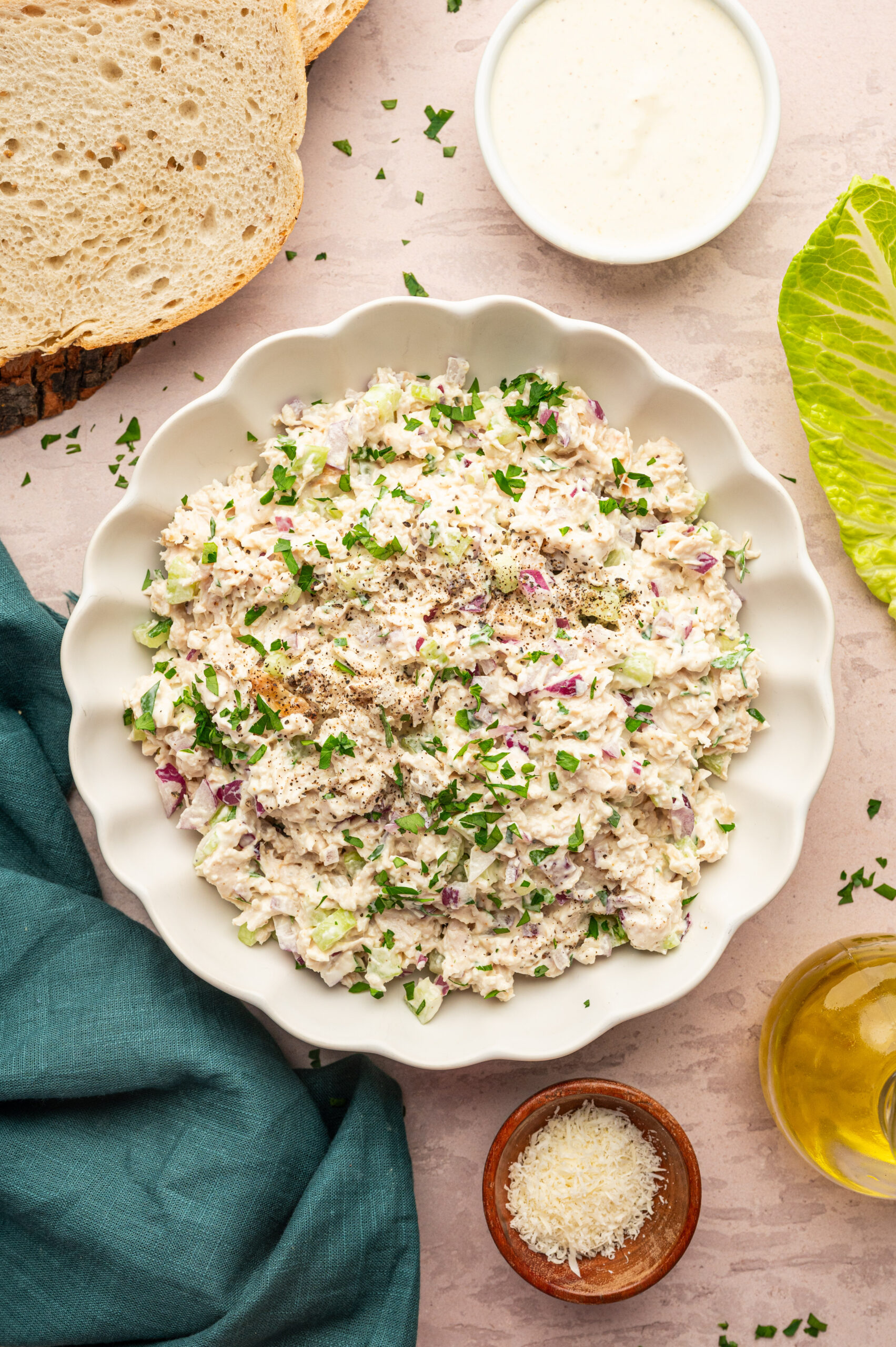 Creamy Caesar Chicken salad in a white serving dish surrounded by ingredients.