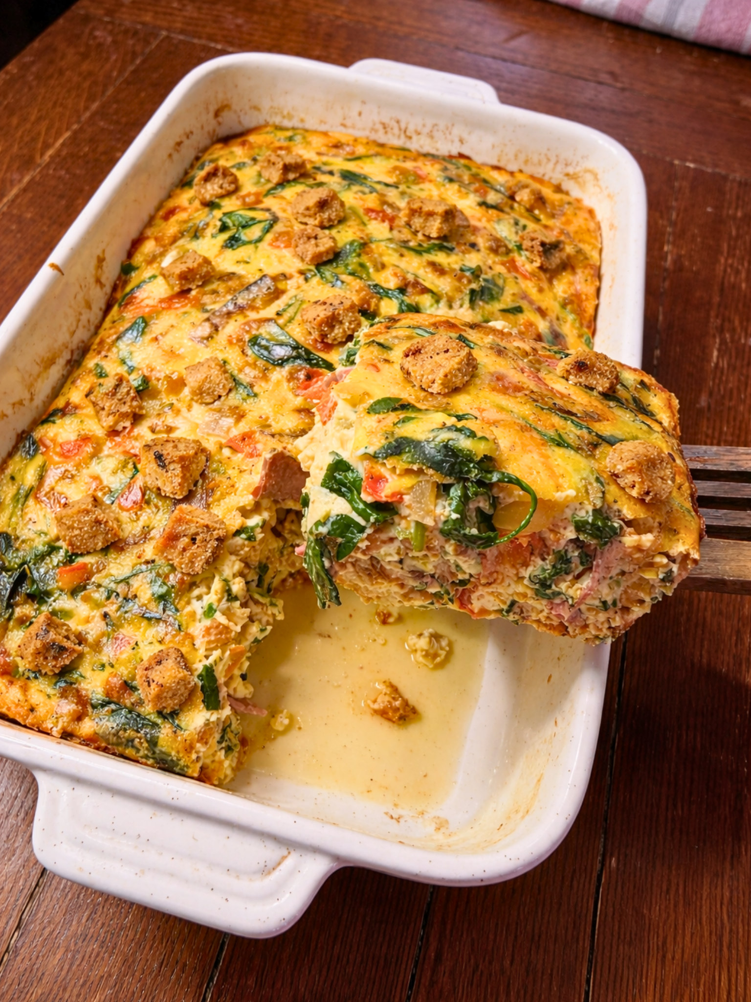 Taking a slice out of a hearty breakfast casserole in a baking dish.
