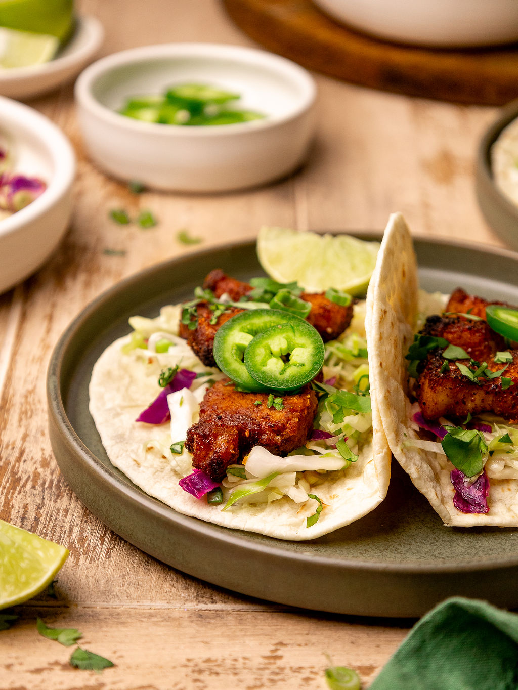 A serving of pork belly tacos topped with jalapenos and lime wedges.