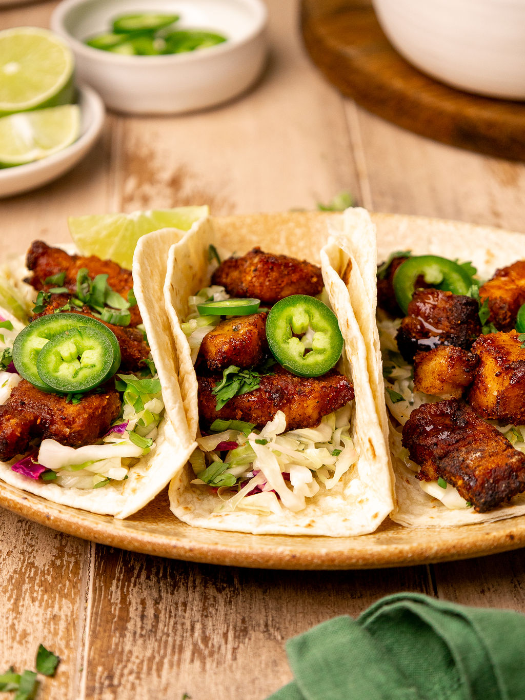 A serving of pork belly tacos topped with jalapenos and lime wedges.