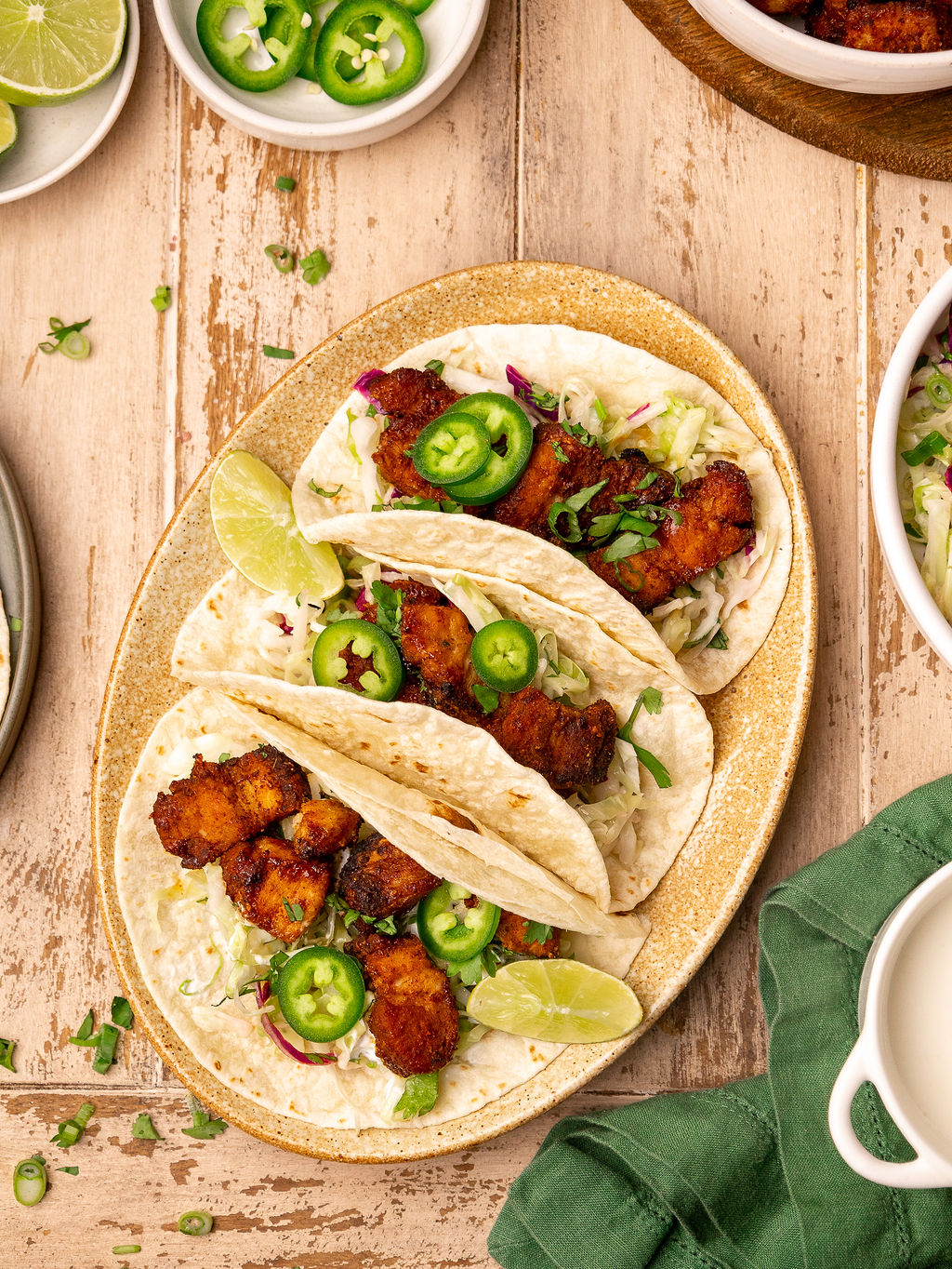 Pork belly tacos on a serving plate topped with jalapenos and lime wedges.