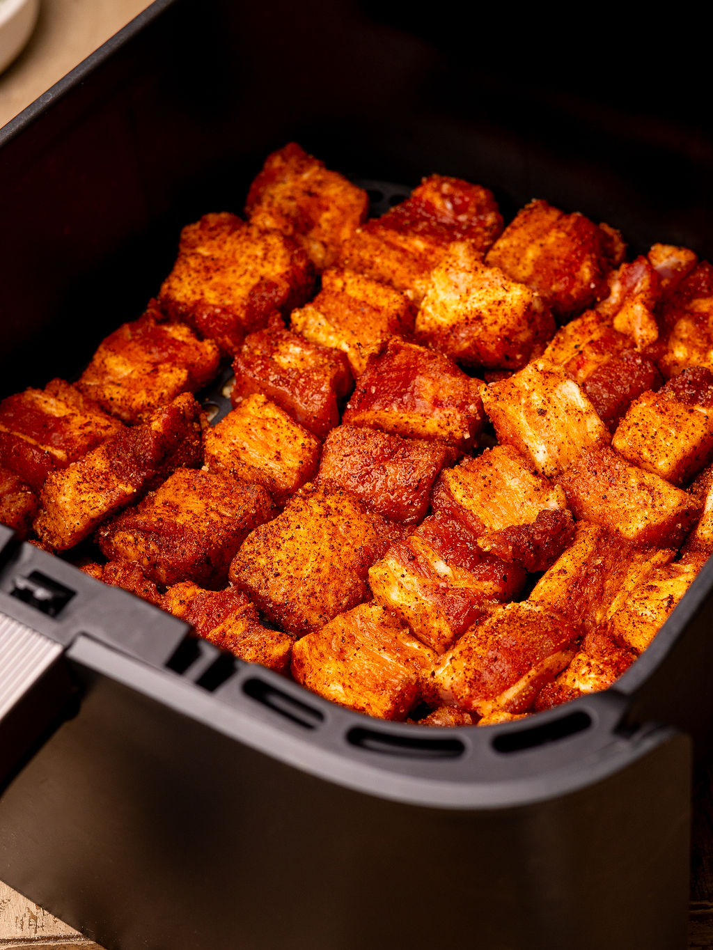 Raw, seasoned pork belly pieces in an air fryer ready to cook.