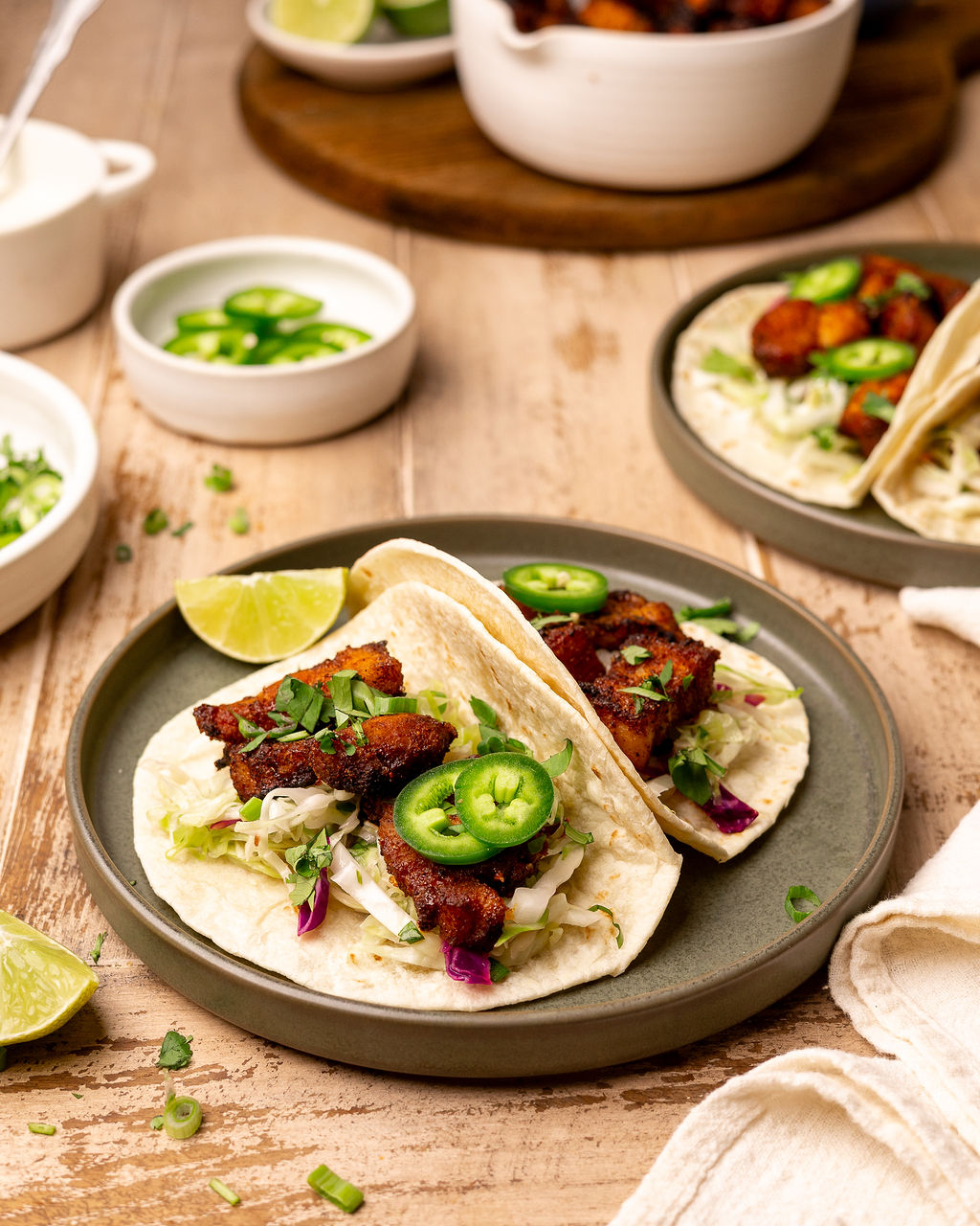 Two pork belly tacos on a plate with toppings.