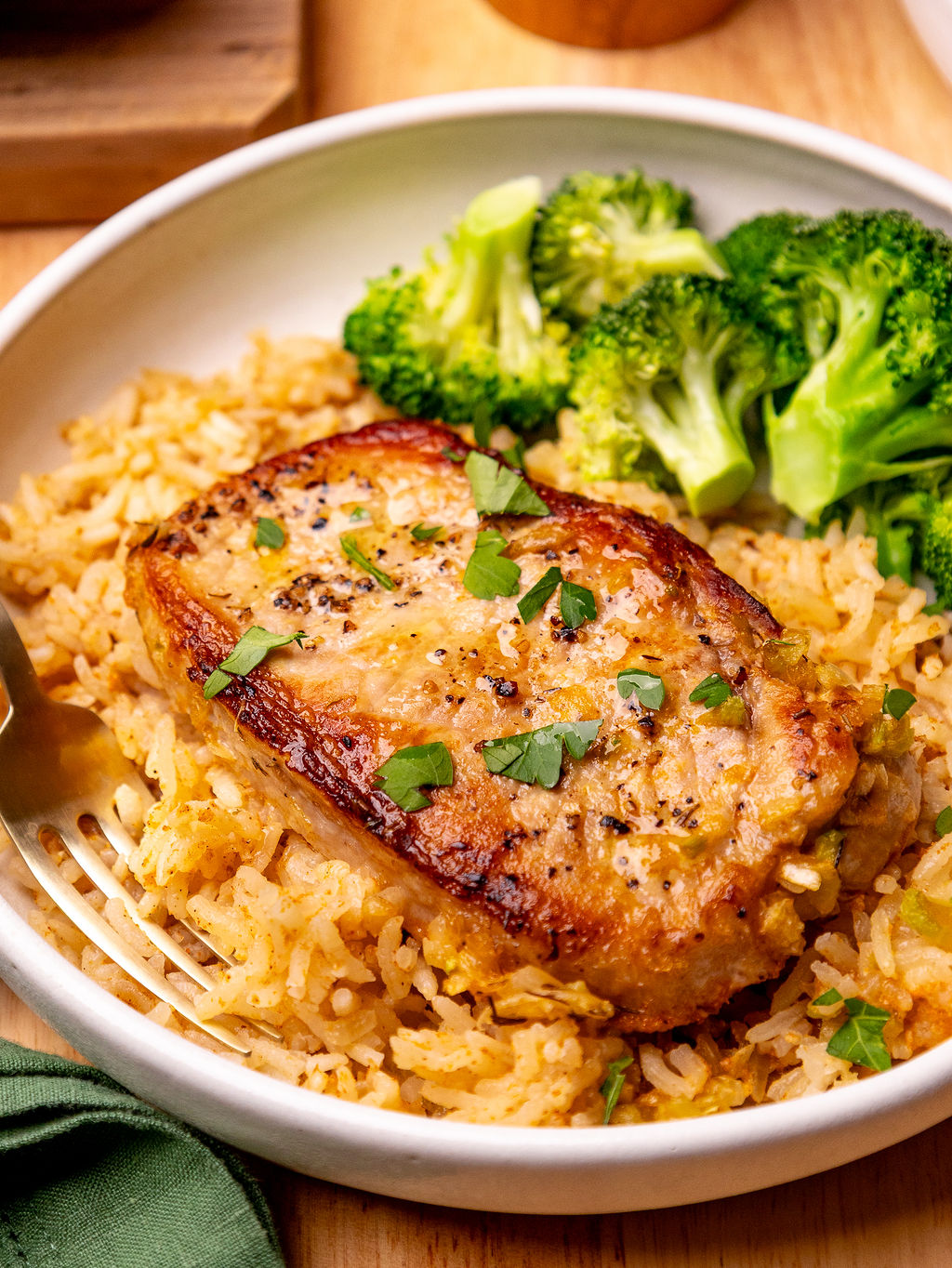 Close-up of pork chop and rice casserole on a white plate with a side of broccoli.