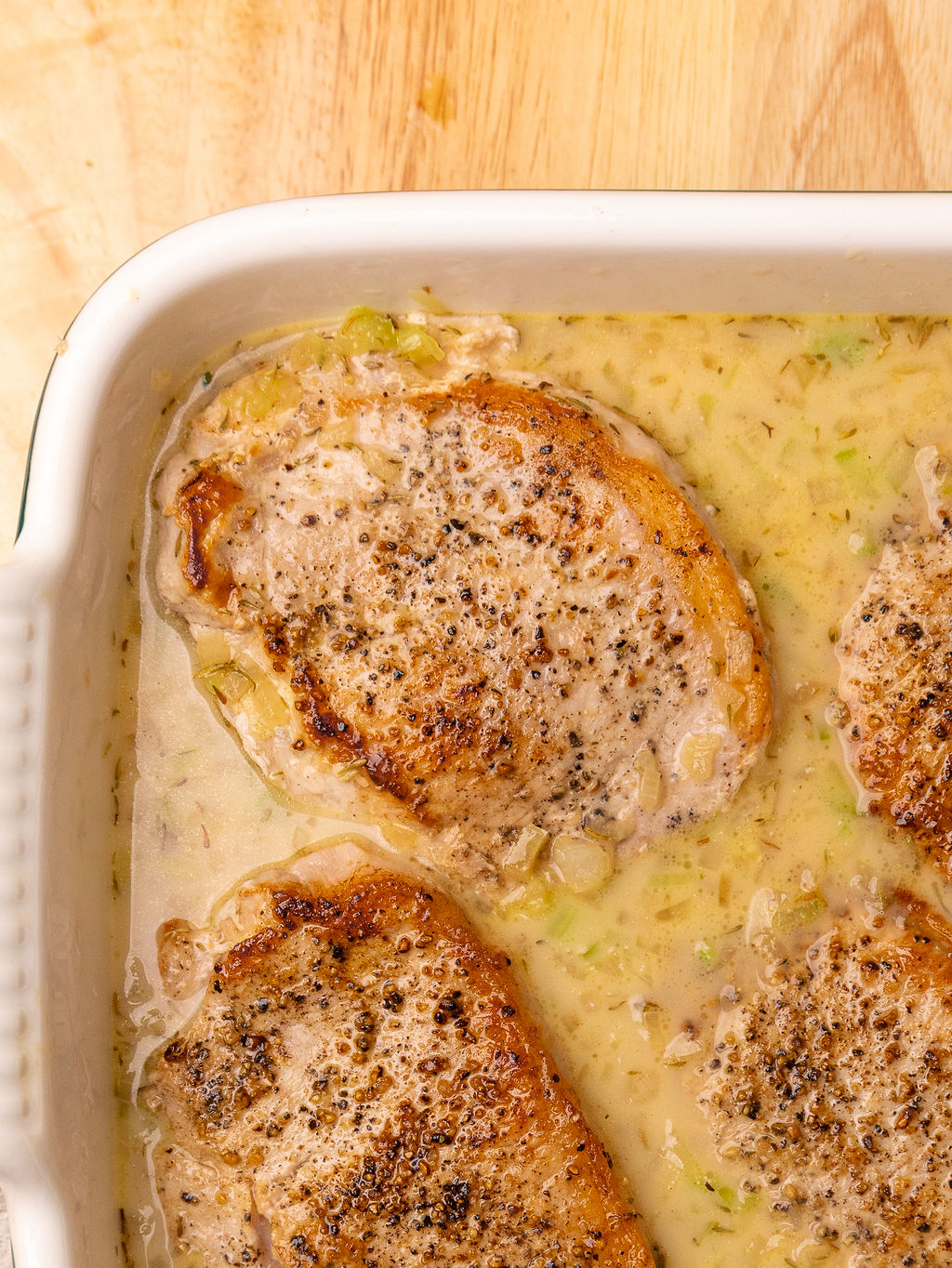 Seared pork chops in a white casserole dish bathing in a buttery sauce.