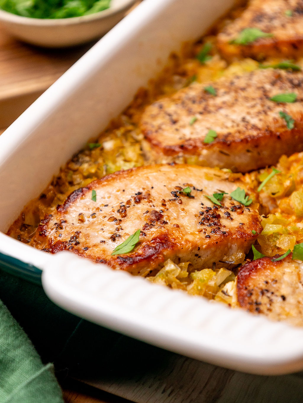 Close-up of pork chops in a white casserole dish with rice and garnished with parsley.
