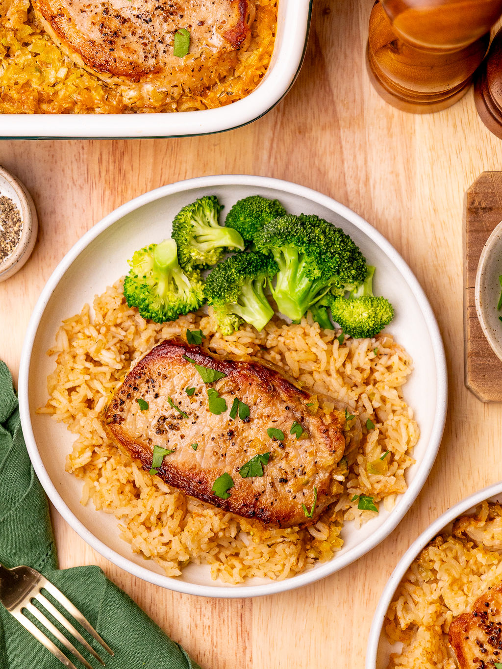 Pork chop and rice casserole with a side of broccoli over a wooden surface.