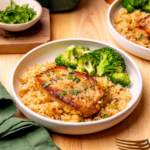 A serving of my pork chop and rice casserole on a white plate with a side of broccoli.